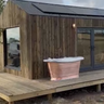 Modern garden cabin with vertical wood cladding and copper bathtub on a wooden deck